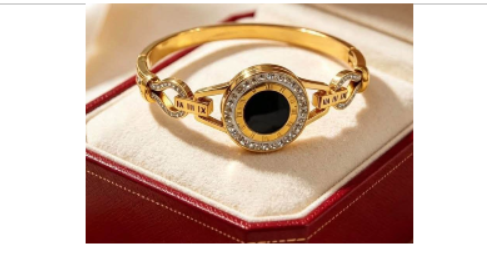 Goldfarbenes Roman Numeral Luxury Armband mit schwarzem rundem Mittelstein und klaren Steinen auf einem Schmuckkästchen